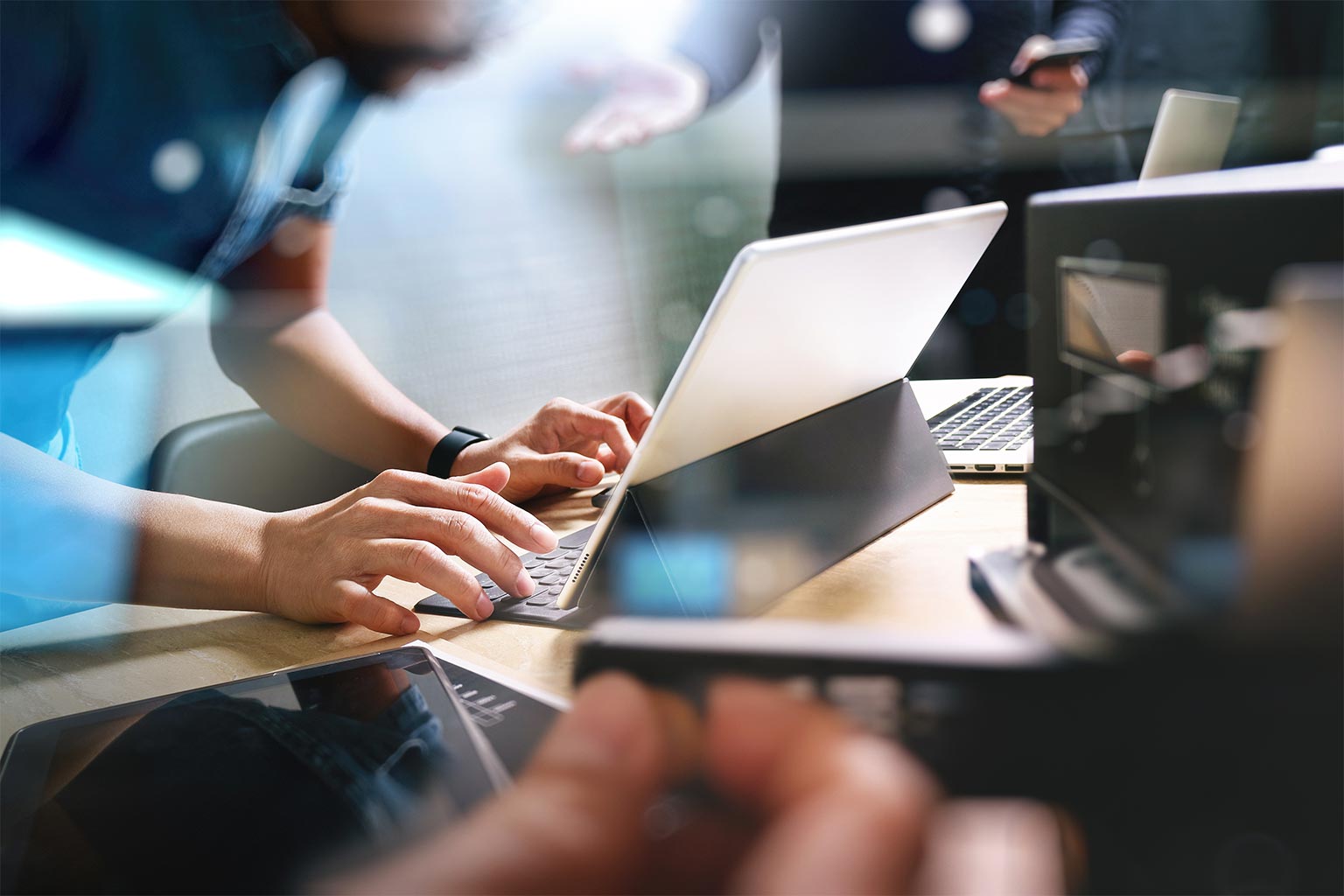 Coworkers using laptops and a tablet at a shared office desk, illustrating IT management for small businesses