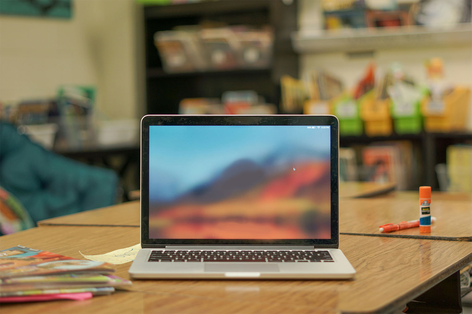 Laptop open on a classroom desk with school supplies, representing K-12 IT device management and summer tech planning